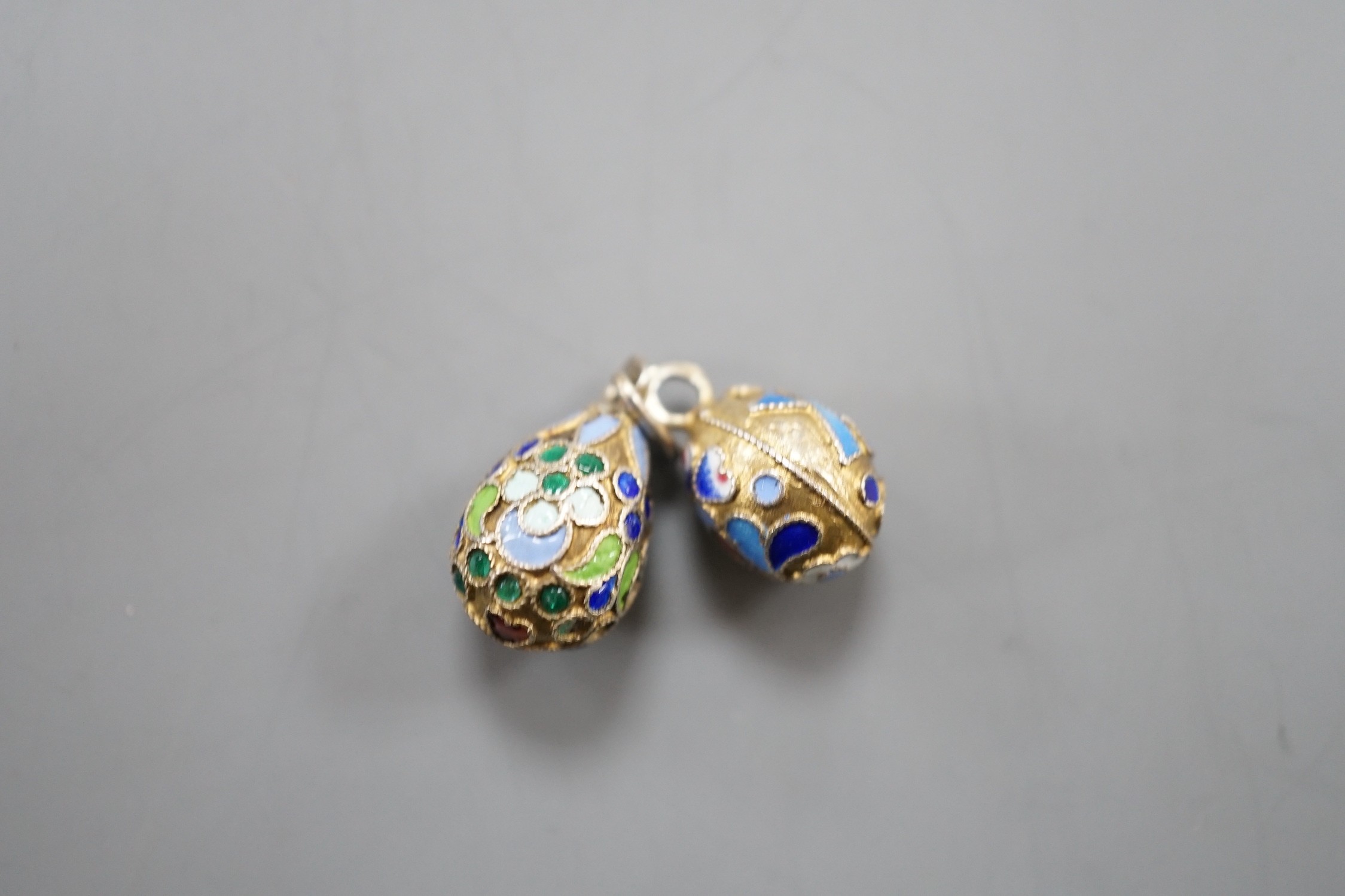 An early 20th century Russian 84 zolotnik and polychrome cloisonné enamel set egg pendant, maker's mark HT?, 17mm and a similar smaller egg pendant, maker's mark HM?.